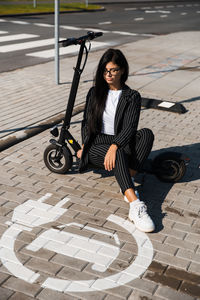 High angle view of woman with push scooter sitting on footpath