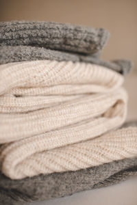 Stack of knitted wool textile sweaters clothes on white blanket in bed at home room close up.