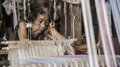 Senior woman weaving loom in factory