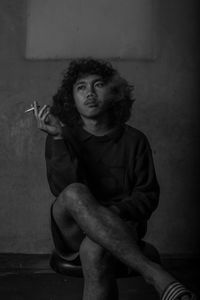 Portrait of man smoking cigarette against wall