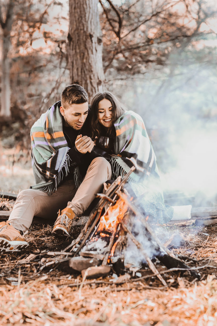adult, two people, men, tree, nature, women, emotion, togetherness, forest, young adult, happiness, burning, lifestyles, fire, smiling, land, positive emotion, friendship, love, plant, female, outdoors, sitting, spring, autumn, leisure activity, clothing, flame, heat, bonding, full length, cheerful, winter, copy space
