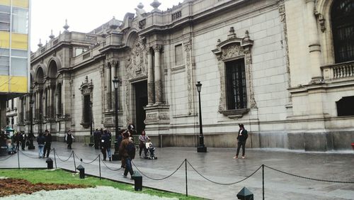 People walking by historic building in city