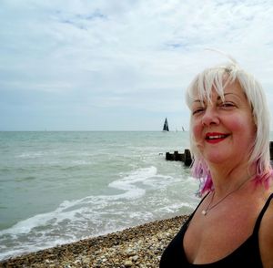 Portrait of smiling mature woman at beach against sky