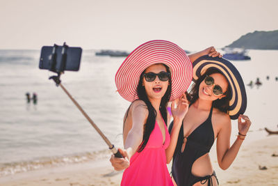 Female friends in hat and sunglasses taking selfie at beach