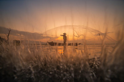 Silhouette man standing on field against sky during sunset