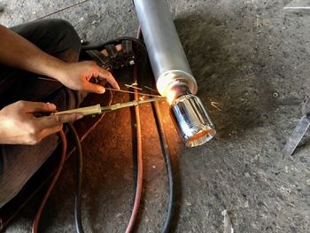 Low section of worker welding exhaust pipe at workshop