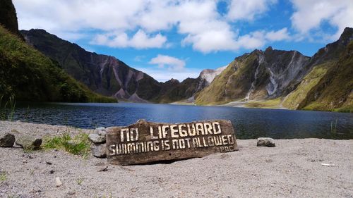 Information sign on rock by lake against sky