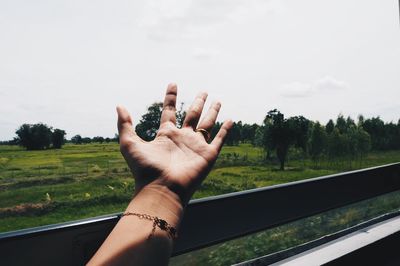 Cropped hand of woman reaching sky through train window