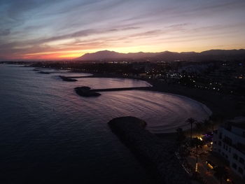 High angle view of sea and cityscape against sky at sunset