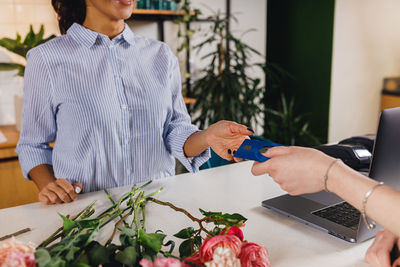 Cropped hand of customer paying at woman at counter in flower shop