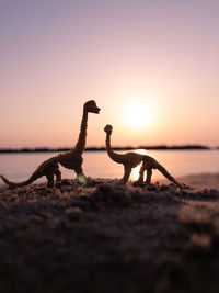 Rear view of dinosaur standing on beach against sky during sunrise