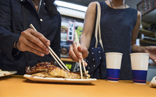 Two friends eating fish at street food market stall in kyoto