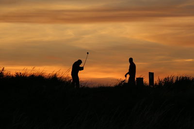 Silhouette men standing on field against sky during sunset