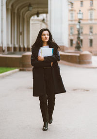 Full length of young woman using phone while standing on building