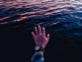 Cropped hand of man wearing wristwatch reaching towards sea during sunset