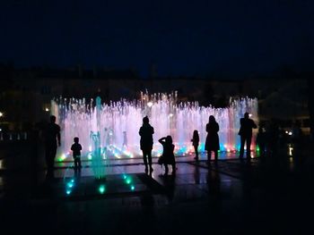 Silhouette people standing against illuminated sky at night