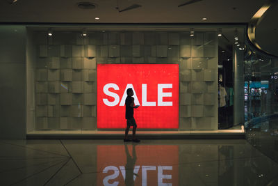 Full length of man standing by illuminated sign on wall