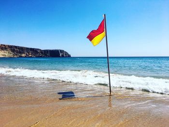 Flag on beach against clear sky