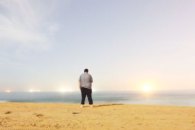 Rear view of man standing on shore at beach against sky