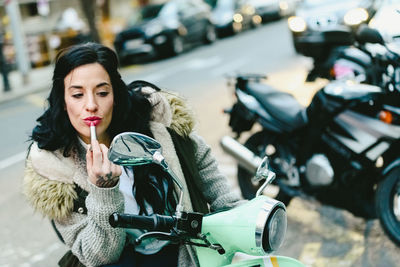 Woman applying lipstick while sitting on motor scooter