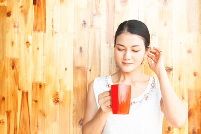 Happy young woman drinking coffee in cup on wood