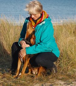 Smiling woman pampering dog on grassy shore