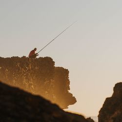 Low angle view of man fishing on rock against sky