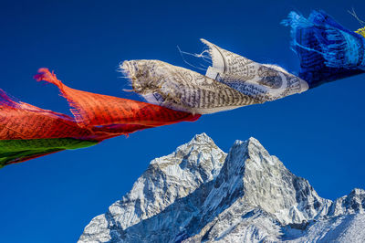 Low angle view of prayer flags and snowcapped mountain against clear blue sky