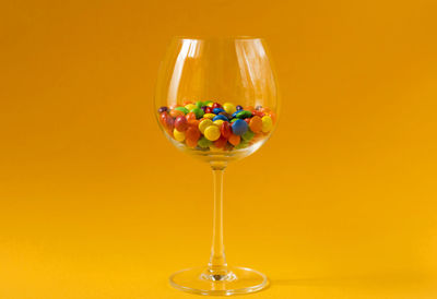 Colorful candies in a wine glass on yellow background