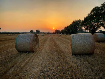 Hay bales on field against sky during sunset