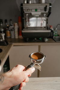 Holds a holder with a tempered coffee tablet against the background of a coffee machine,