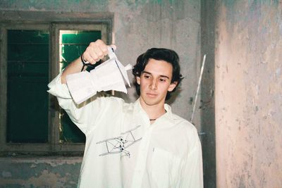 Young man holding kettle standing against old wall