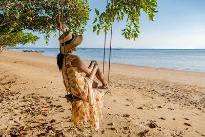 Full length of woman sitting on swing against sea