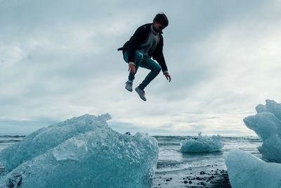 Man jumping in snow against sky