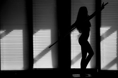 Silhouette woman exercising with pole against blinds