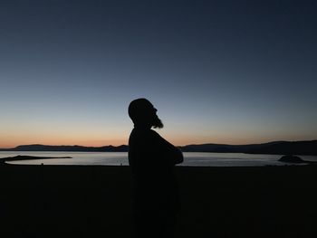 Silhouette man standing at beach against sky during sunset