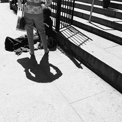 Low section of woman standing by homeless man sitting on sidewalk