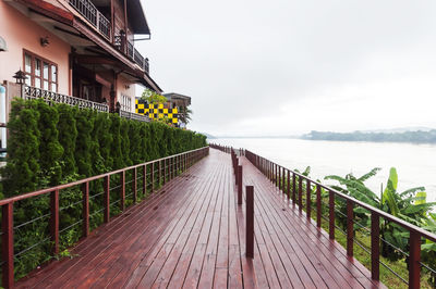 Narrow walkway leading to calm lake against sky