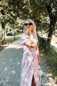 Portrait of smiling young woman wearing sunglasses standing on footpath