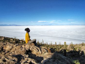 Man sitting on rock looking at sea against sky