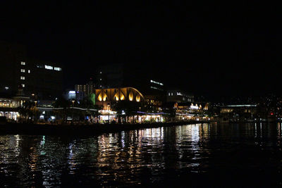 Illuminated buildings by river against sky at night