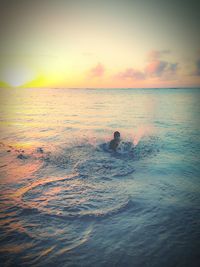 Rear view of silhouette man in sea against sky during sunset