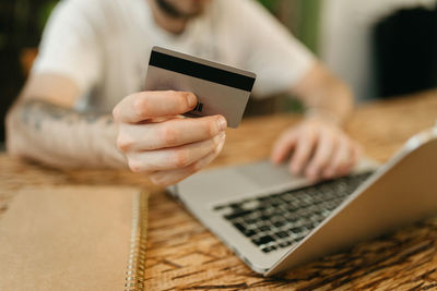 Crop unrecognizable male making purchase with plastic card for order during online shopping via laptop