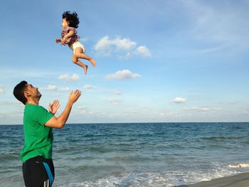 Full length of happy boy jumping on beach against sky