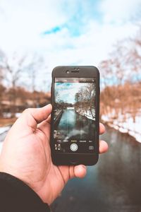 Close-up of man holding smart phone against sky