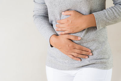 Midsection of woman with stomachache standing against gray background