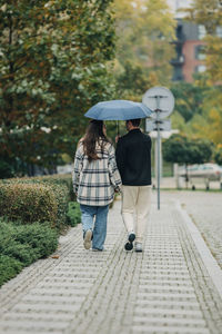 Young couple walking together under umbrella on footpath