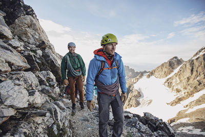 Two rock climbers with helmets and ropes walk along a cliff in tetons