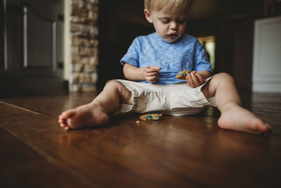 Cute baby boy eating cookie while sitting on floor at home