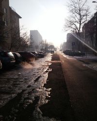 Wet street in city against sky